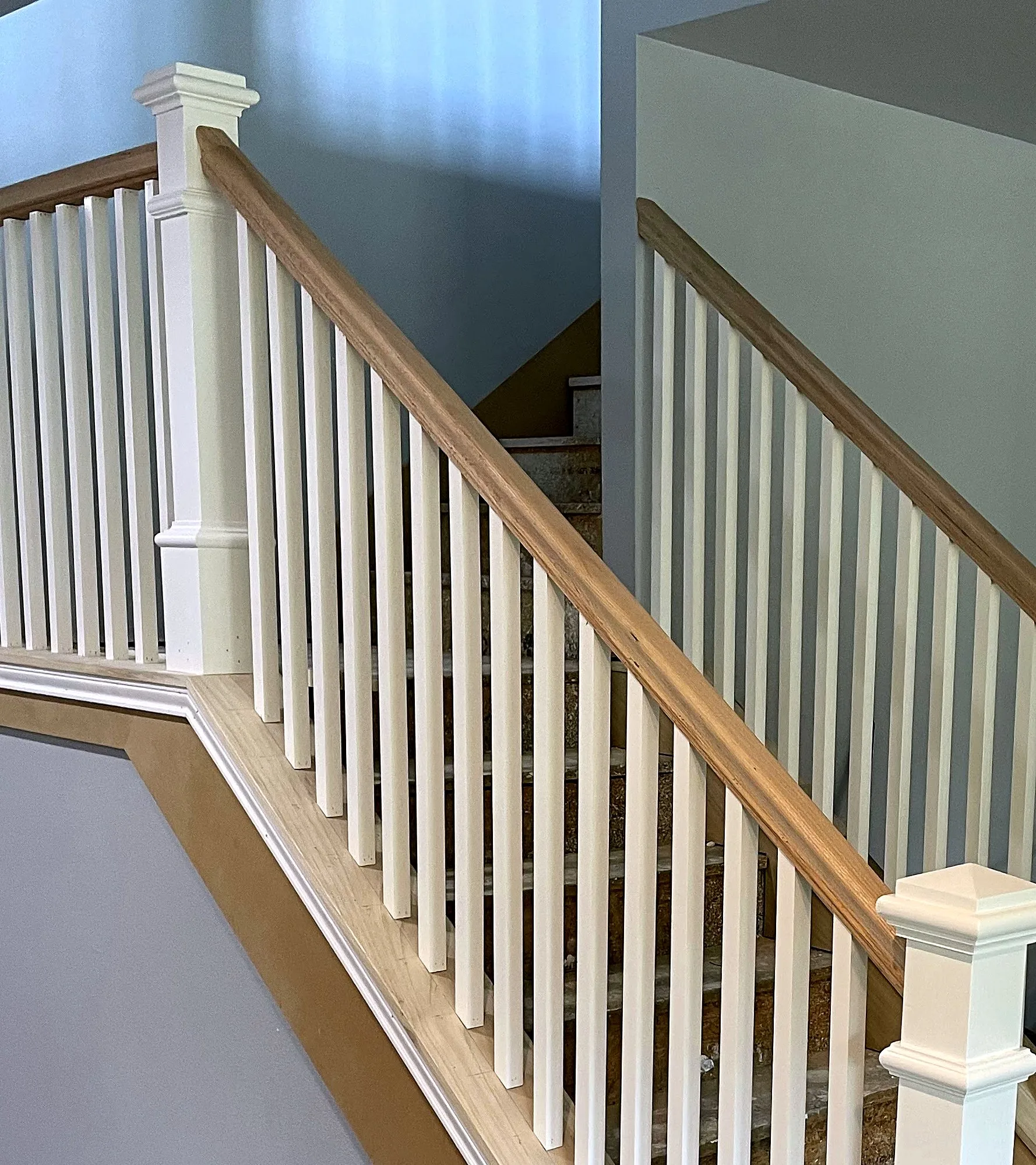 A straight staircase with white painted balusters, an oak handrail, and a square newel post