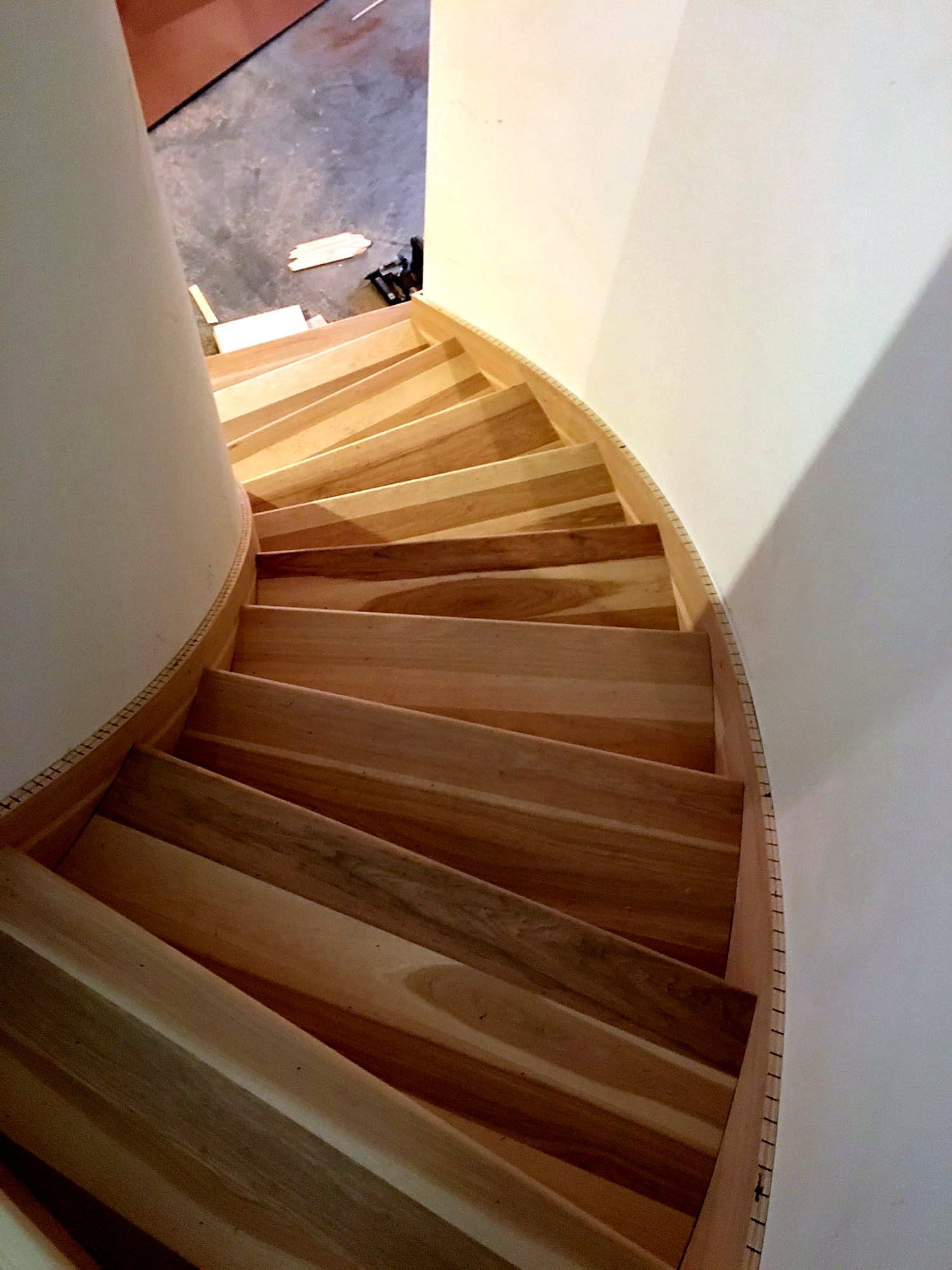 Overhead view of a spiral staircase's finished wood treads in two alternating tones, curving down to a lower landing