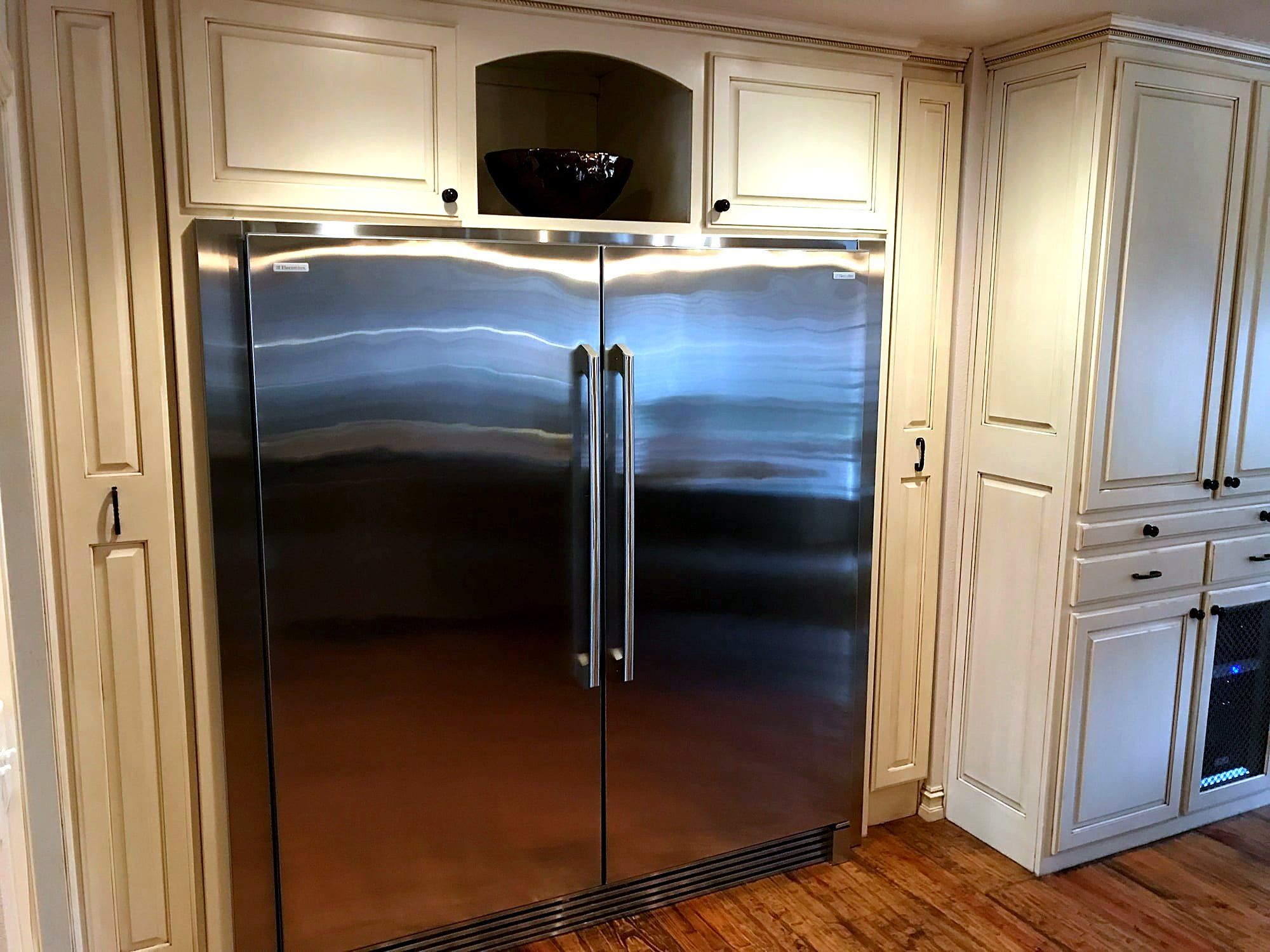 Built-in stainless steel refrigerator flanked by floor-to-ceiling cream cabinetry