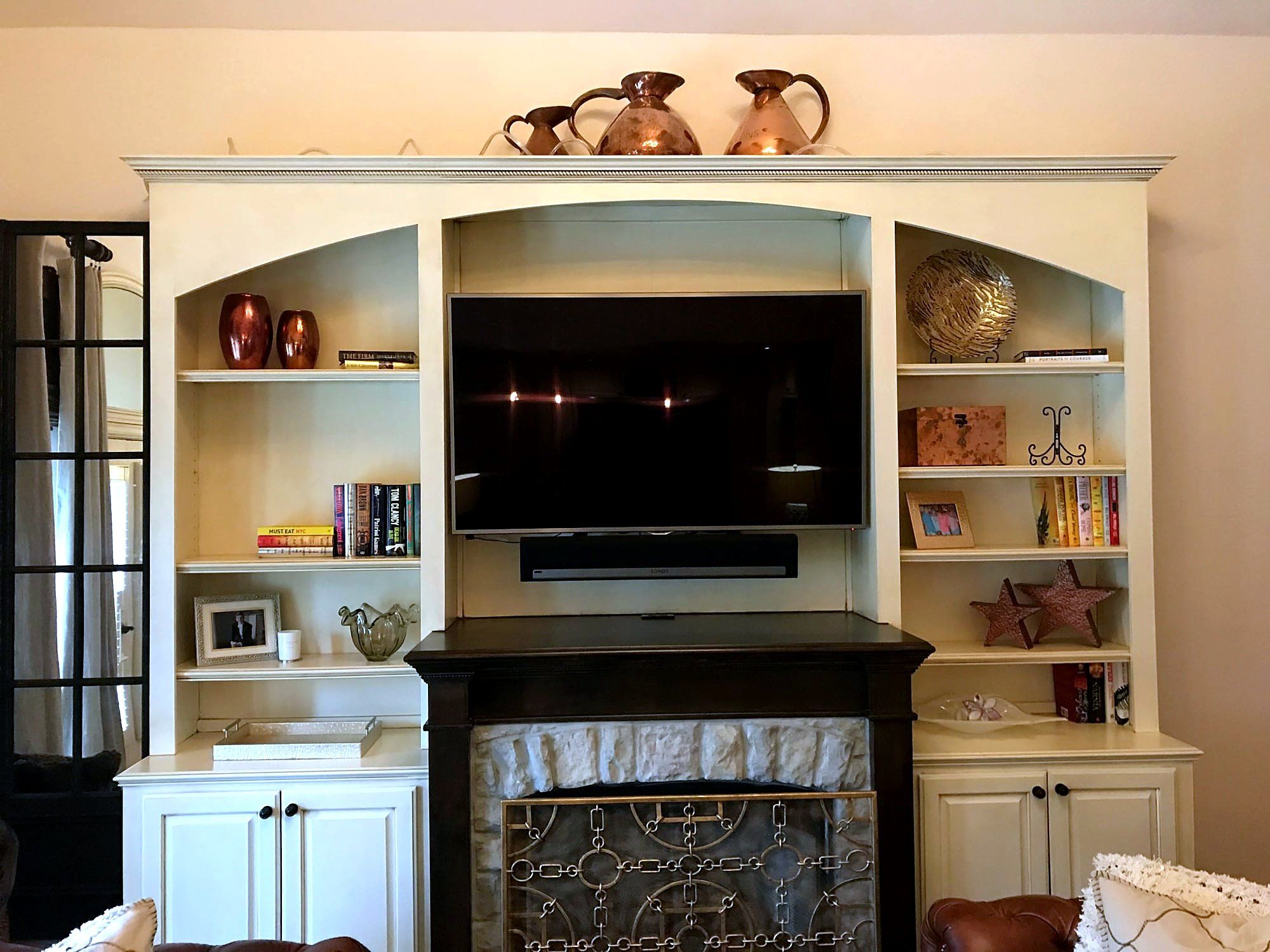 Cream-painted built-in wall unit with a fireplace, mounted television, and flanking bookshelves