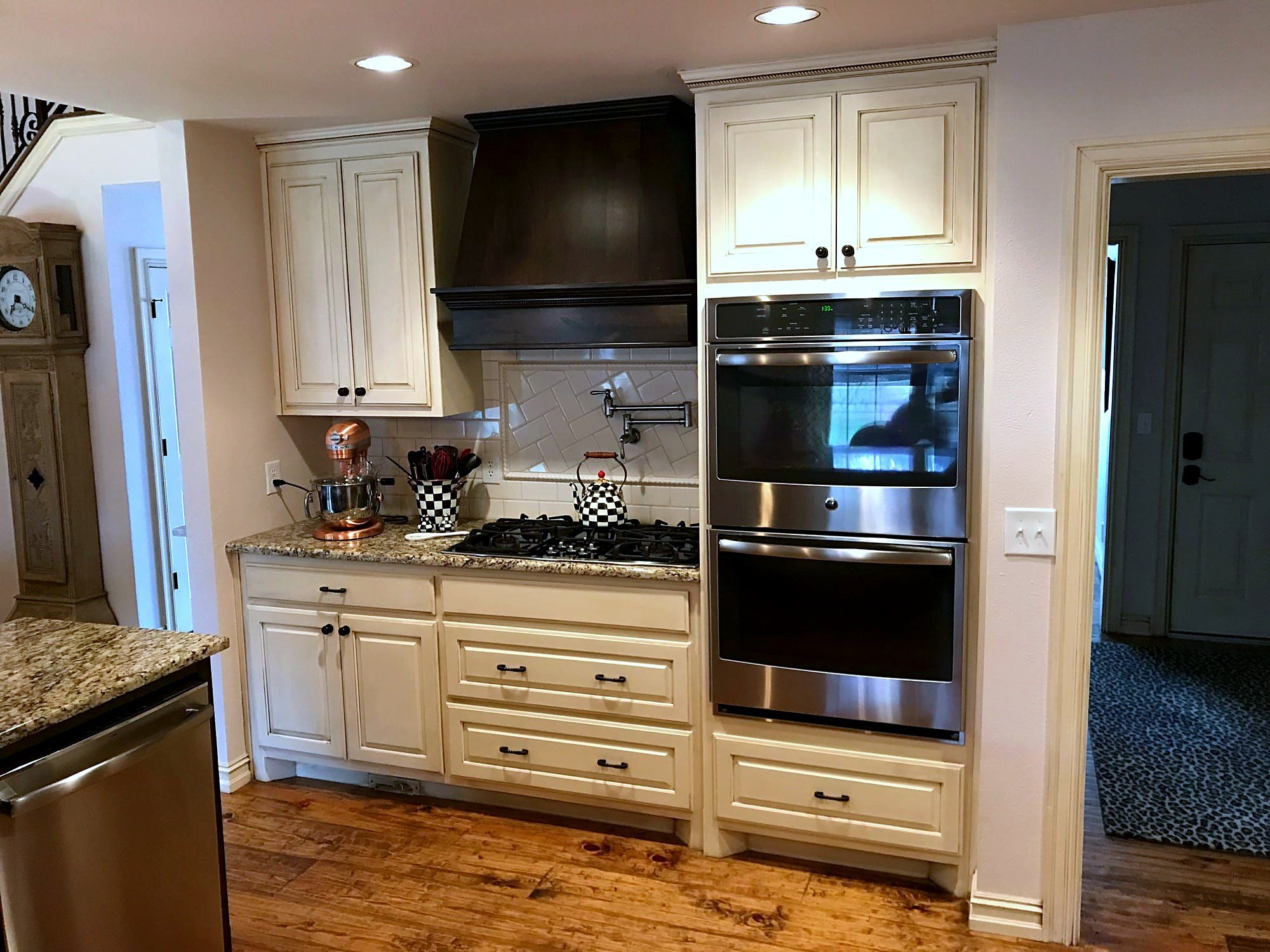Cream kitchen cabinetry with a dark wood vent hood, stainless double ovens, and hardwood floors