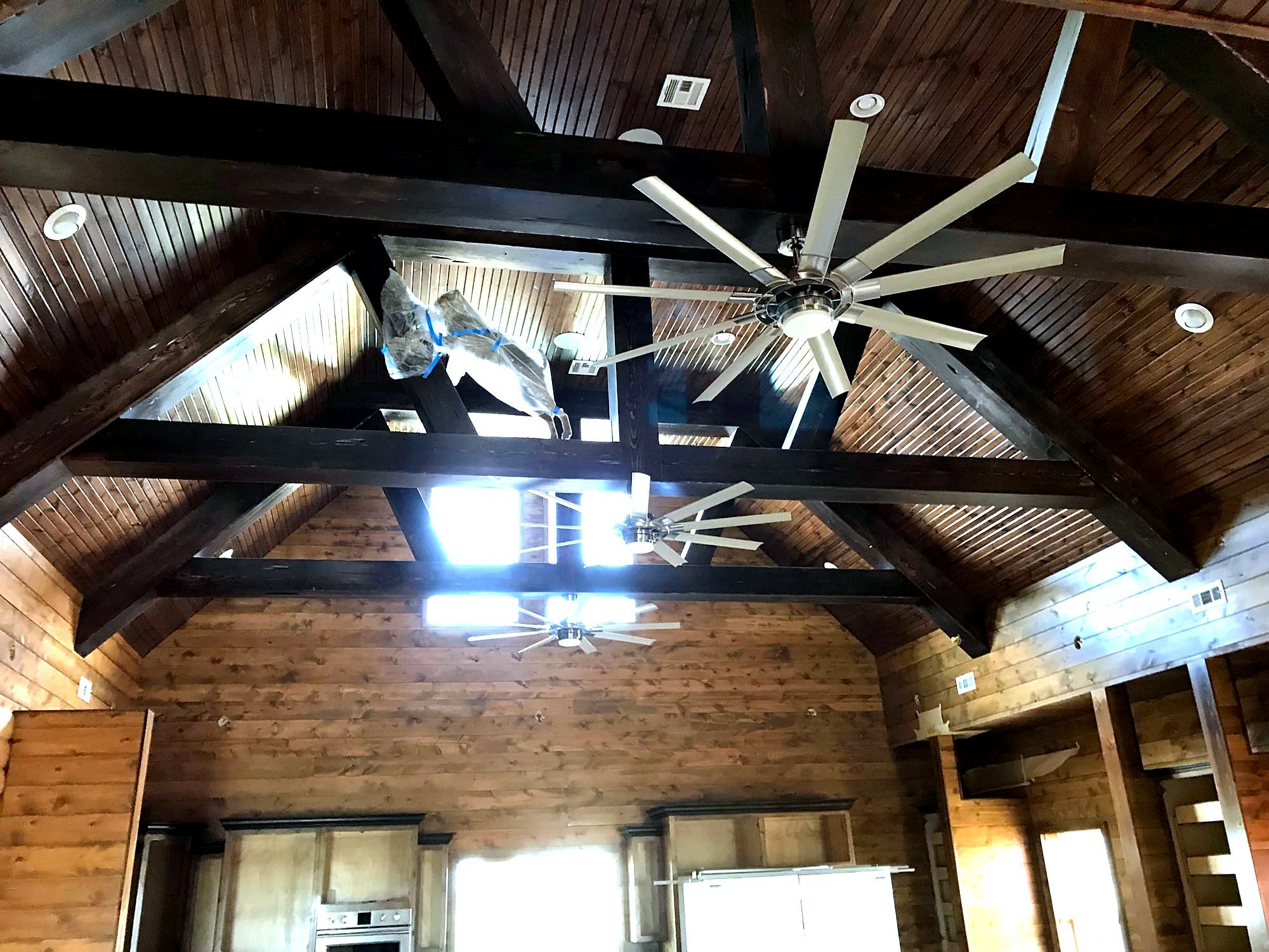 Upward view of exposed wood king-post trusses with a large ceiling fan and skylights