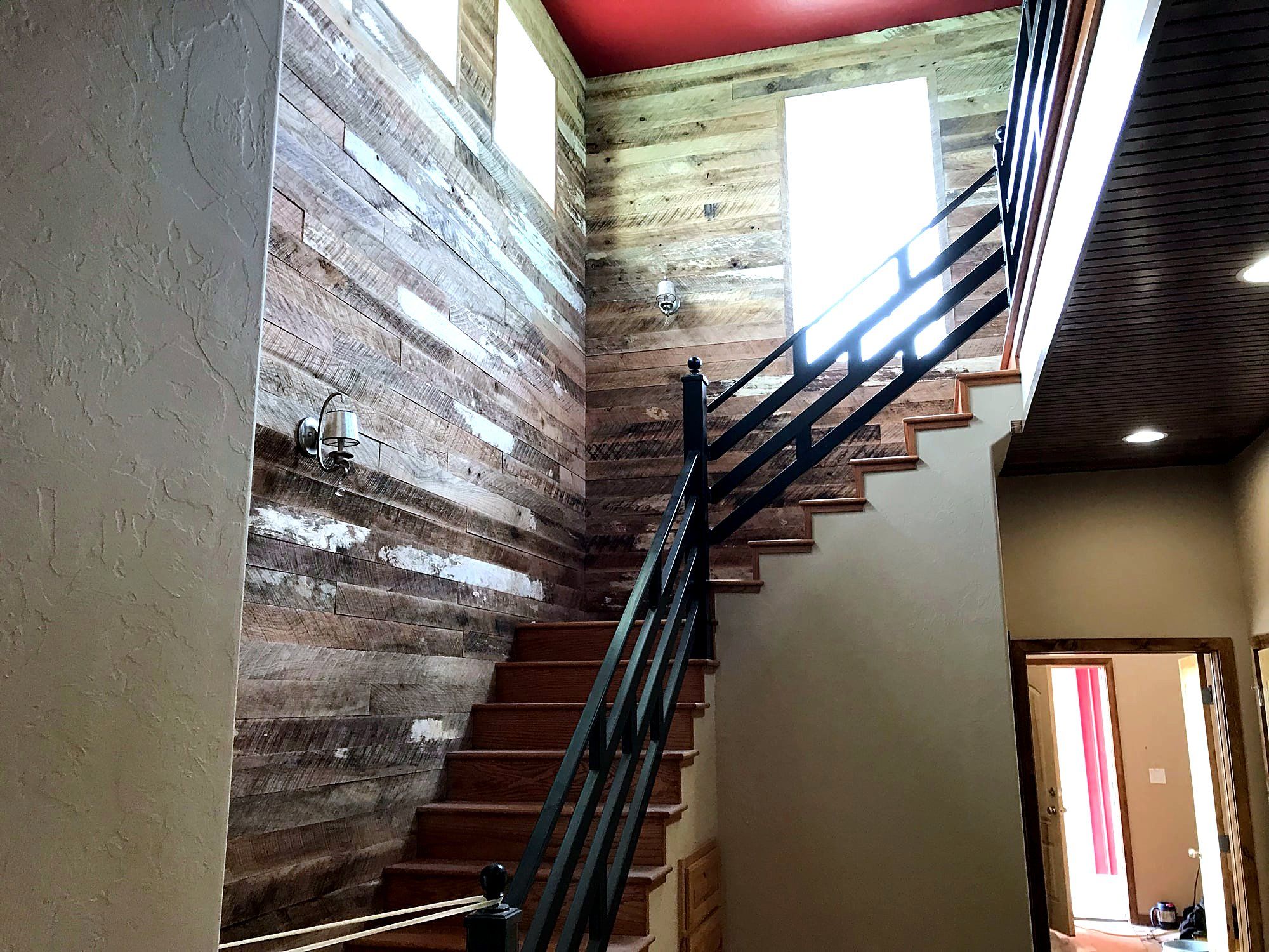 Reclaimed wood plank accent wall beside a staircase with a black iron handrail