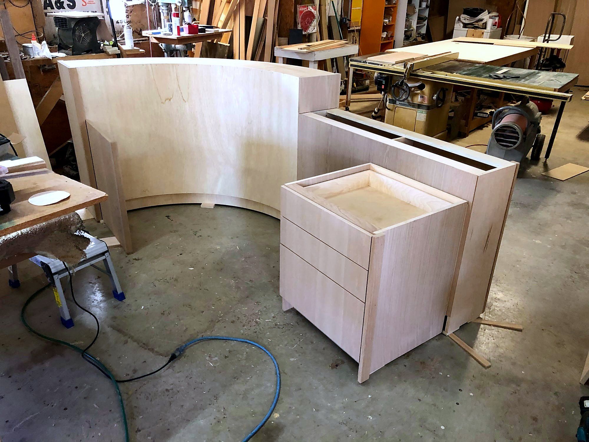 Curved bar cabinet front bent to a tight radius in birch plywood, paired with a rolling drawer base unit, mid-assembly in the shop