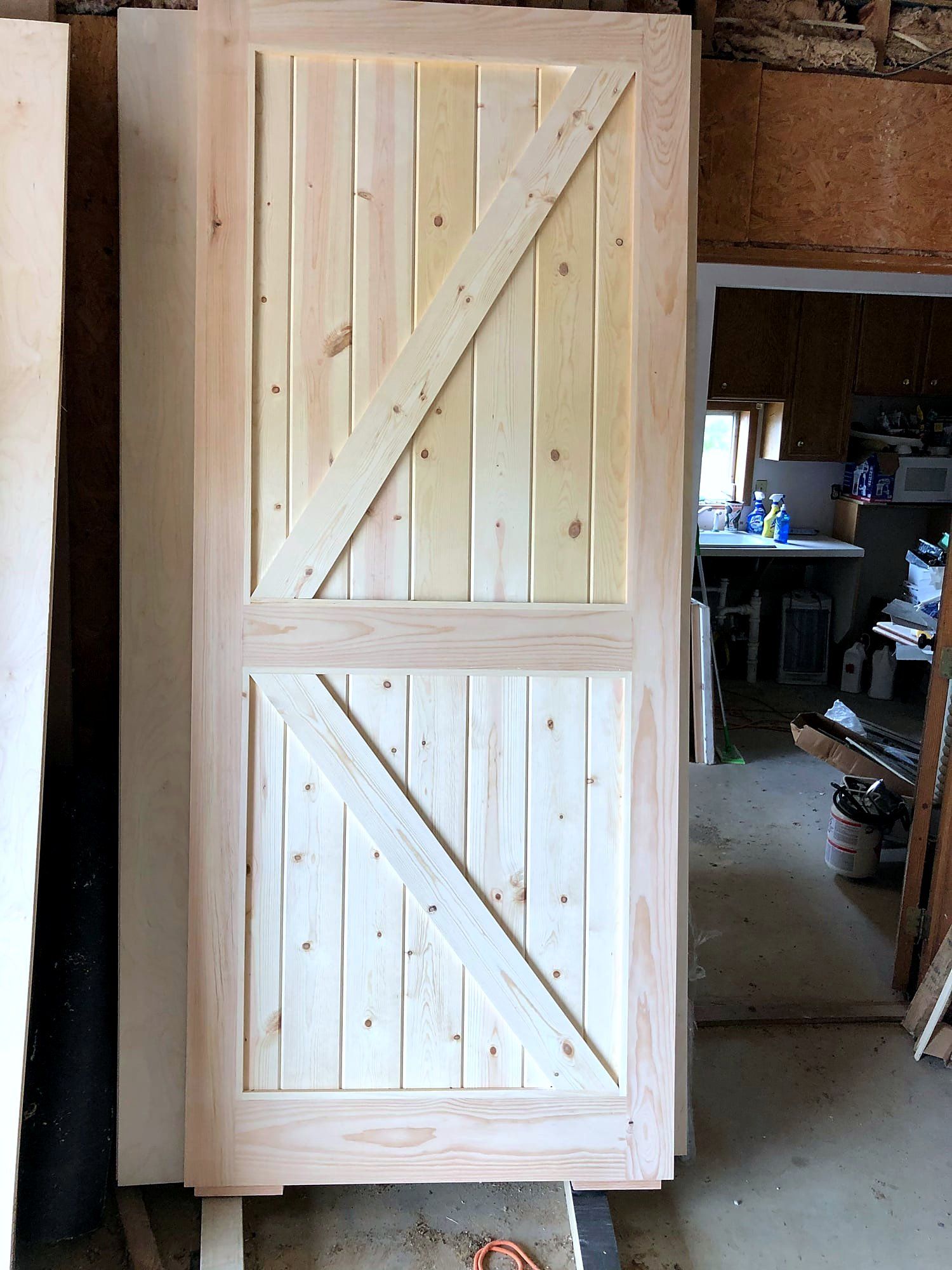 Knotty pine barn door with a bold Z-brace pattern top and bottom, sanded and ready to hang, a finished kitchen visible through the doorway behind it