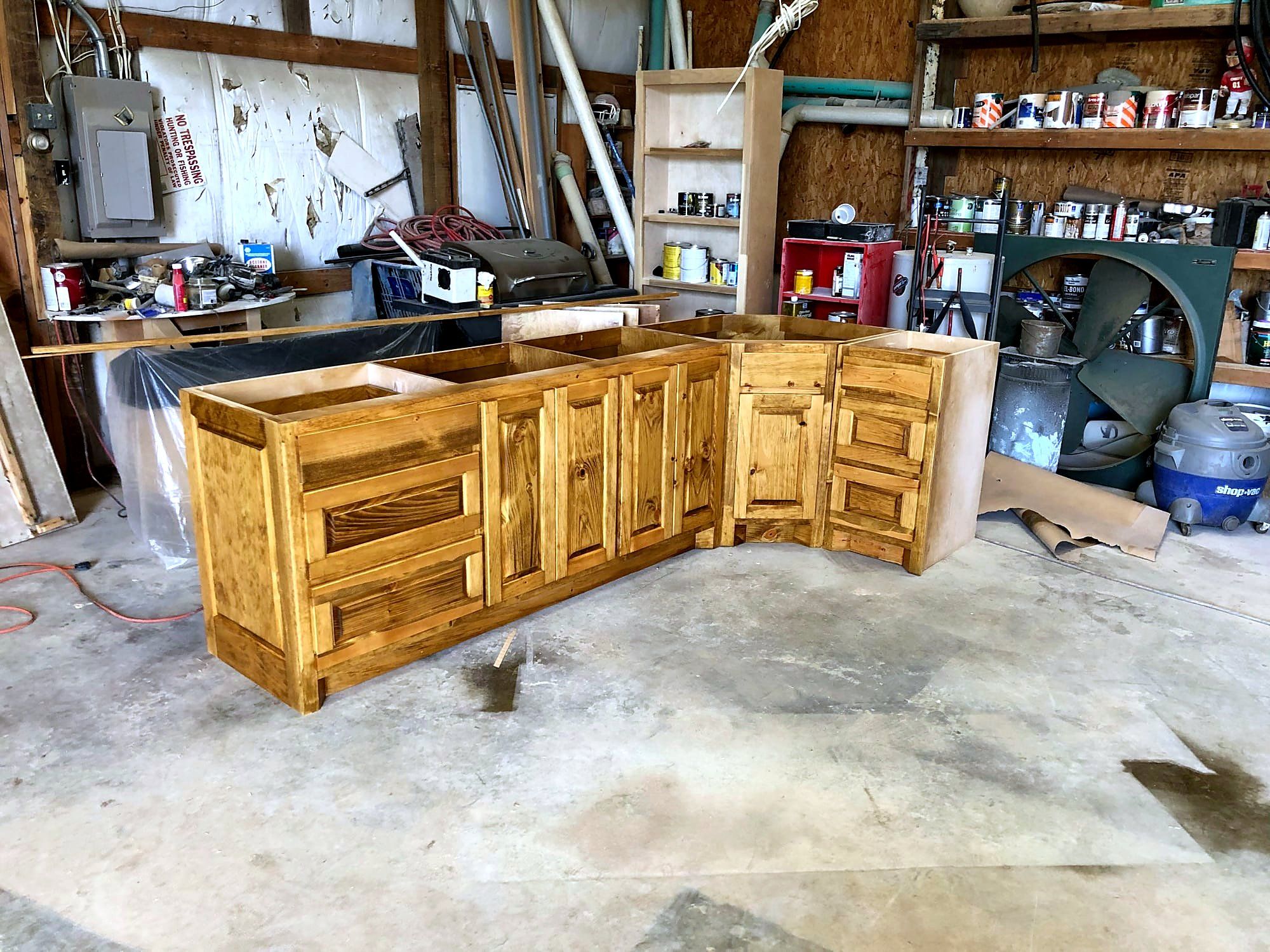 L-shaped vanity cabinet run with an angled corner unit, honey-stained raised-panel doors and drawers, staged in the shop before delivery