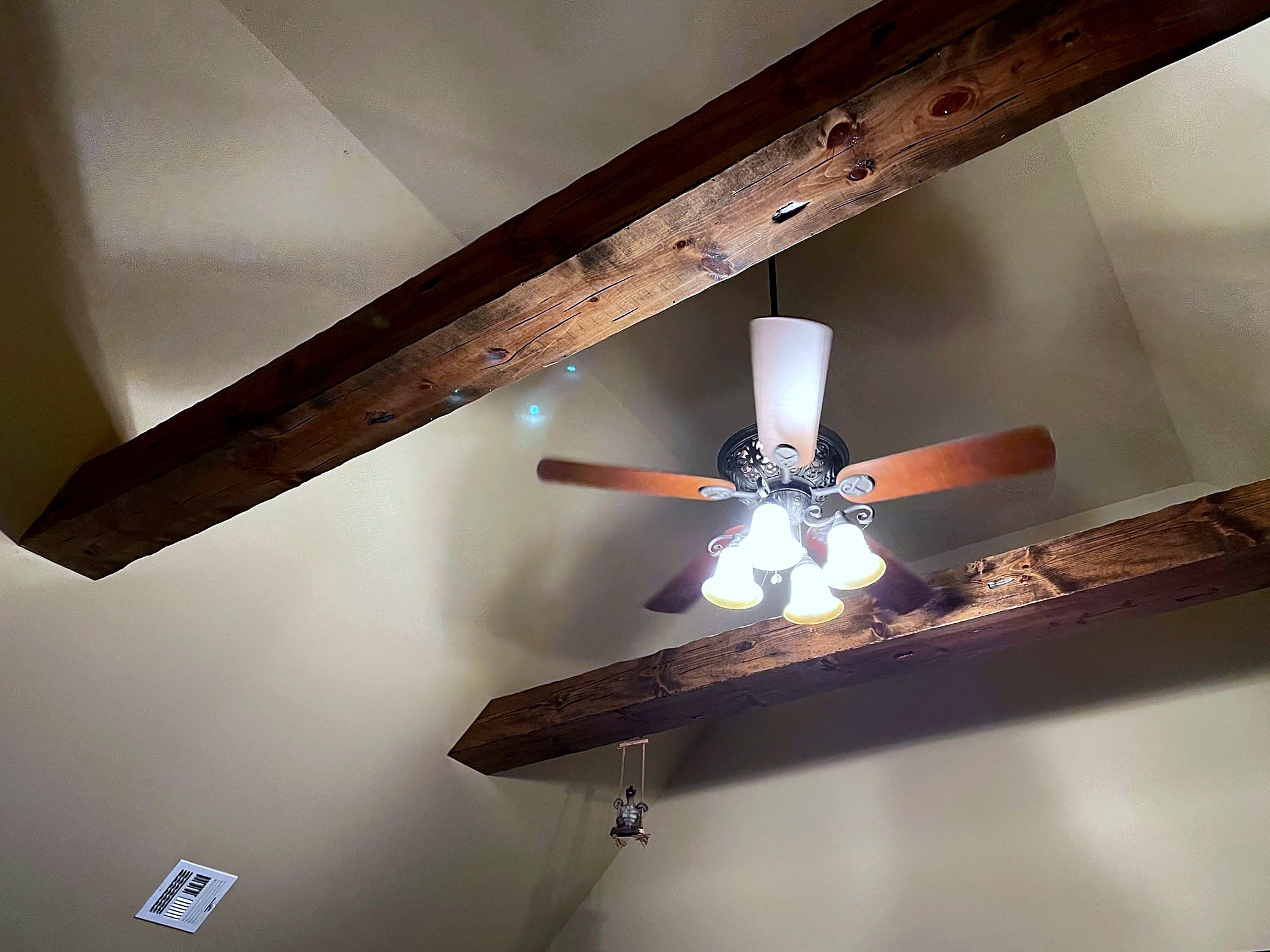 Exposed wood ceiling beams crossing in an X pattern above a mounted ceiling fan