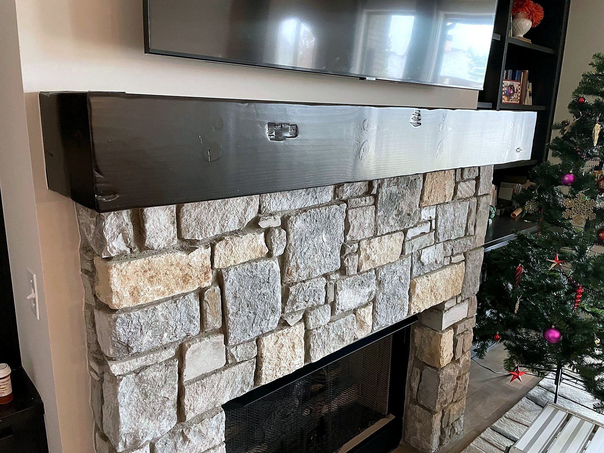 Stone fireplace with a rustic wood mantel beam and a television mounted above