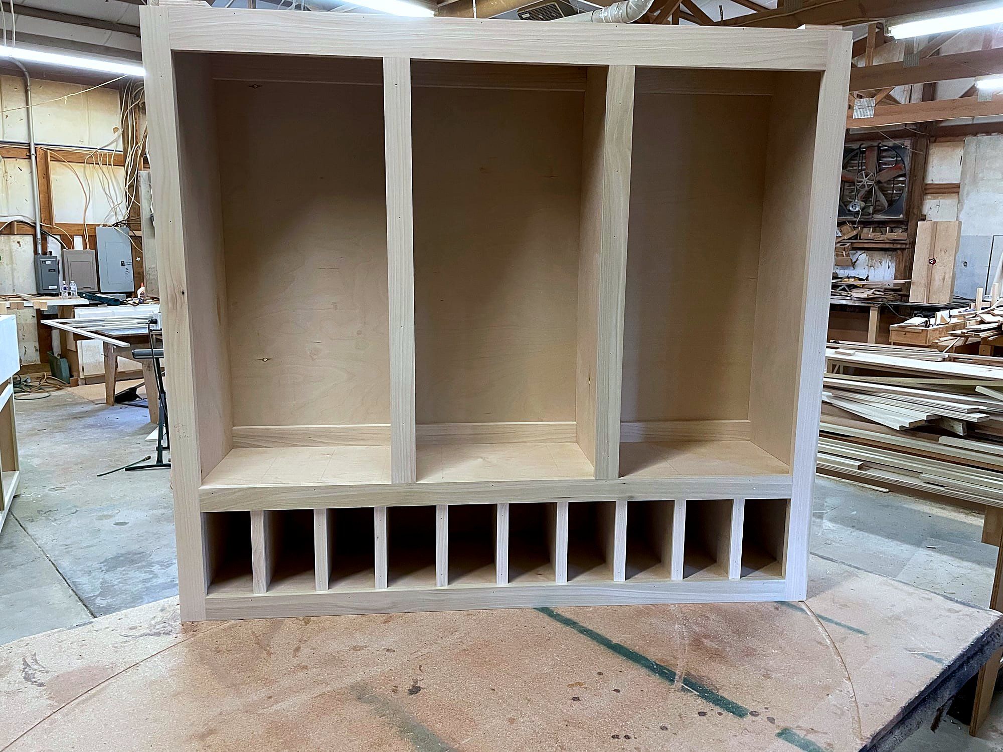 Mudroom locker carcass with three open cubbies above a row of shoe slots, unstained pine, built in the shop