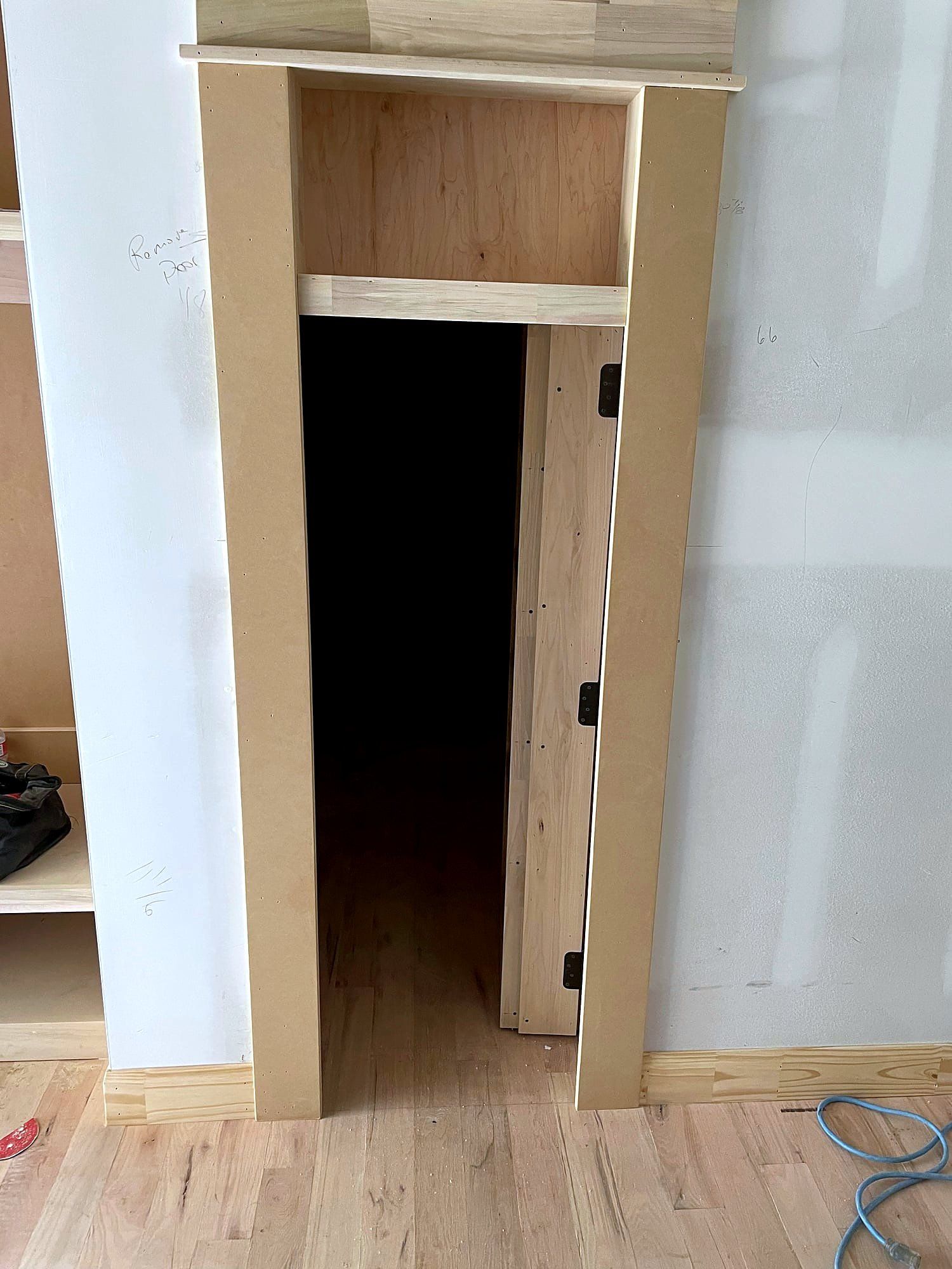 Cased doorway opening with mitered pine casing and a paneled door hung on butt hinges, leading into an unfinished closet