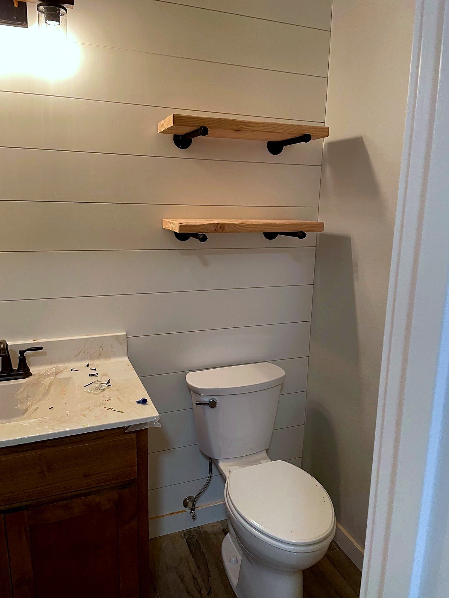 Powder room with shiplap walls, a wood vanity, and floating wood shelves on pipe brackets