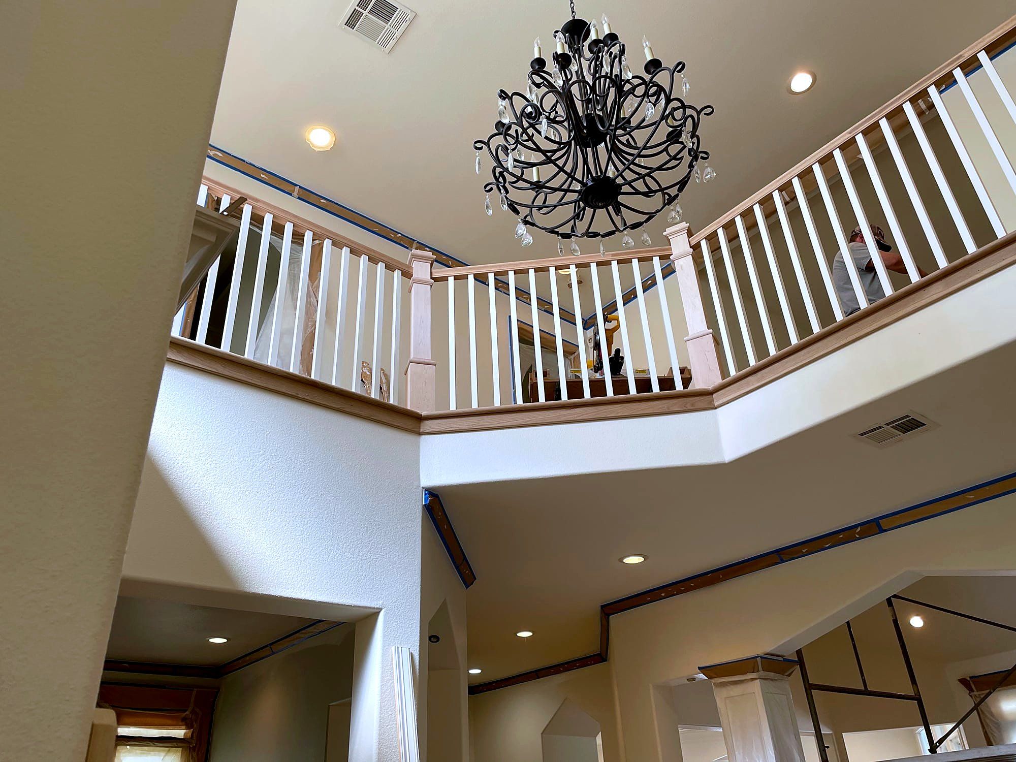 Two-story stairwell with a wood handrail, white balusters, and a wrought iron chandelier
