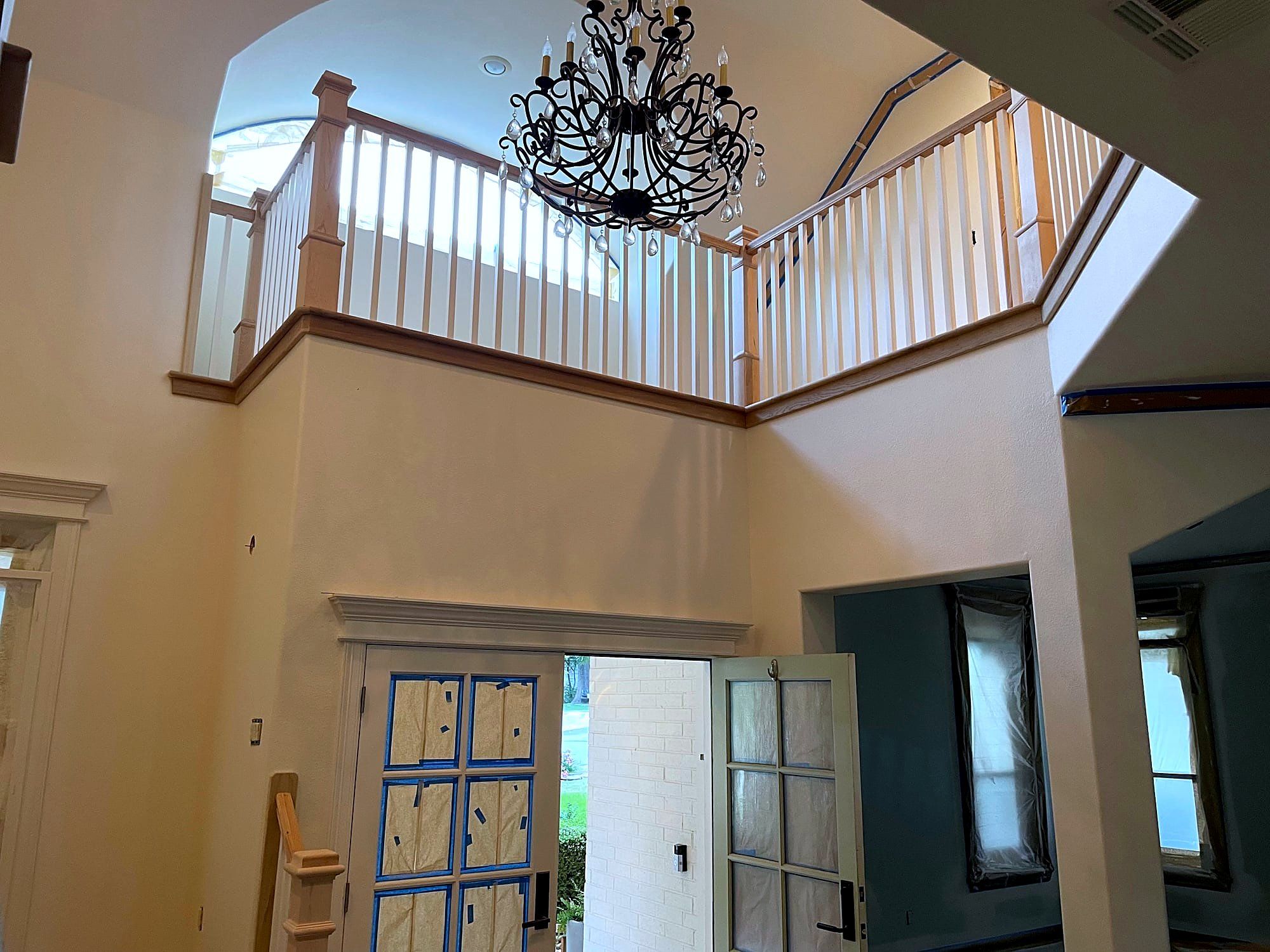 Two-story stairwell with a wrought iron chandelier and an arched doorway below