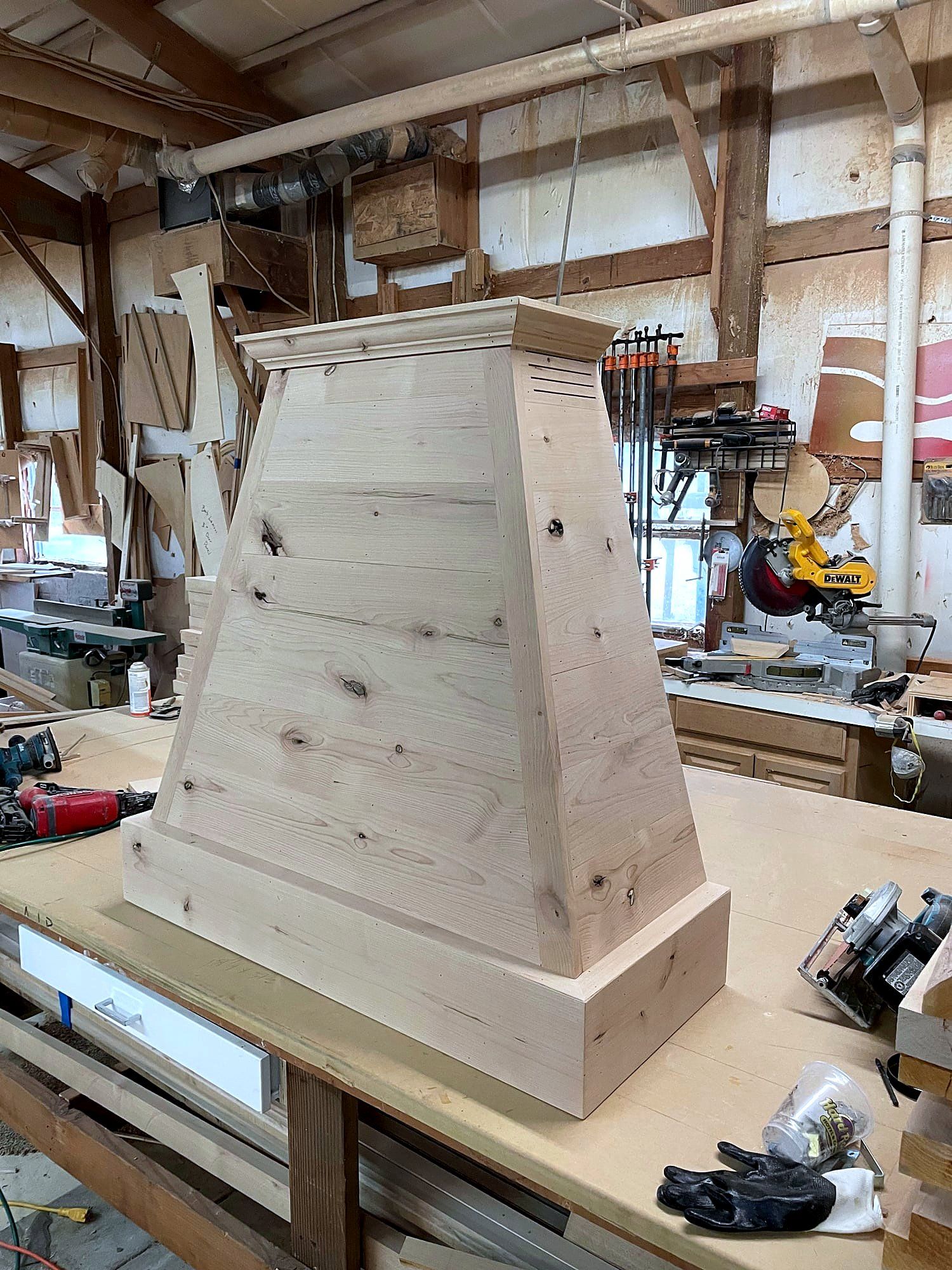 Tapered wood range hood with a crown cap and cross-grain banding, built and sanded on a shop workbench, ready for install